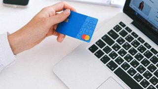 Bezahlung & Befreiung Person sitzt vor Laptop und hält eine Kreditkarte in der Hand